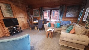Un acogedor interior de cabaña de madera con un sillón azul, un sofá color beige y una mesa de comedor con sillas.