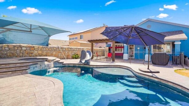A swimming pool with a slide, a covered seating area, and a stone wall.