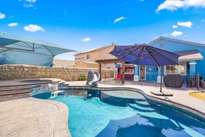 A swimming pool with a slide, a covered seating area, and a stone wall. - Mini Resort! Come enjoy the cool blue colors and ocean 🌊 style feel of our home (El Paso)