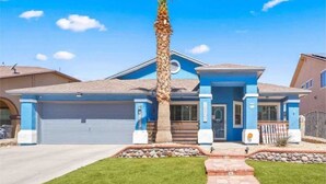 A residential house with a blue exterior, a garage, a well-maintained lawn, and a palm tree.