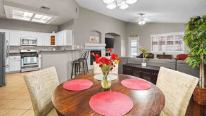 A modern kitchen with white cabinets, a dining table with red placemats, and a vase with flowers.