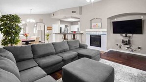 A modern living room with a grey sectional sofa, a flat-screen TV mounted on the wall, and a fireplace.