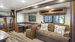 Ein kompaktes Wohnmobil-Interieur mit einer Küchenzeile, einer mit floralen Kissen versehenen Sitzecke und einem Essbereich.