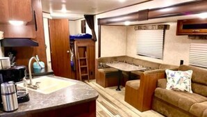 Ein kompaktes Wohnmobil-Interieur mit Küchenzeile, Essbereich und Sitzgelegenheit.