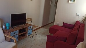 A living room with a TV on a wooden stand, a red sofa, and a white chair. - Marsalforn flat near beach and boulevard (Zebbug)