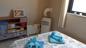 A room with a wooden cabinet with multiple compartments, a standing heater, a window with a view, and a table with folded towels. - Marsalforn flat near beach and boulevard (Zebbug)