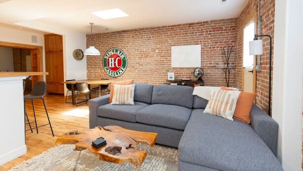 A living room with a grey sofa, a wooden coffee table, and a brick wall. - Downstream Loft - Historic Savory Building (Salida)