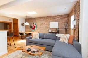 Un salon avec un canapé gris, une table basse en bois et un mur en briques.