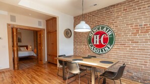 A dining area with a wooden table and chairs, a hanging light fixture, and a brick wall with a Sinclair HC Gasoline sign. - Downstream Loft - Historic Savory Building (Salida)