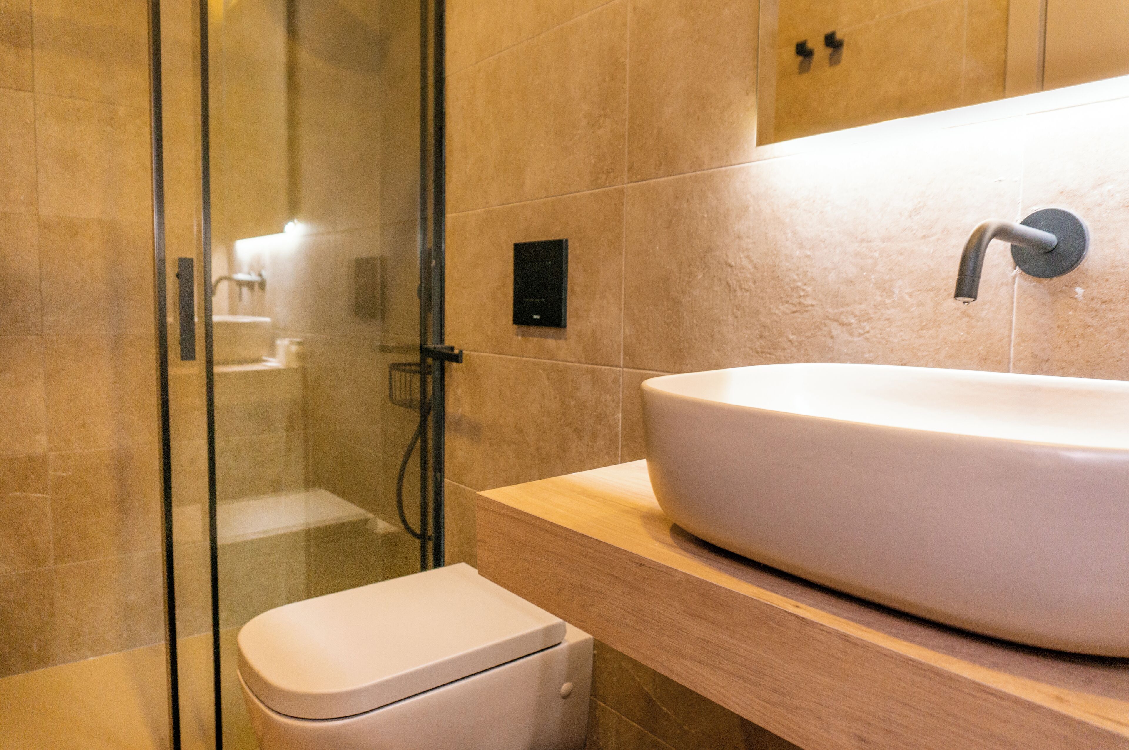 Un baño moderno con un lavamanos grande y blanco, cabina de ducha con mampara de vidrio y un inodoro.