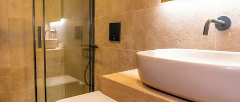 Un baño moderno con un lavamanos grande y blanco, cabina de ducha con mampara de vidrio y un inodoro.