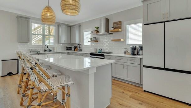 A modern kitchen with white cabinetry, a large island, wicker chairs, and pendant lights. - Seaside Splendor! Rooftop Views, 3 Minute Walk to Beach (Carolina Beach)