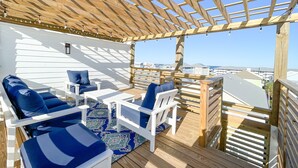 A covered outdoor seating area with wooden furniture and a view of the city. - Seaside Splendor! Rooftop Views, 3 Minute Walk to Beach (Carolina Beach)