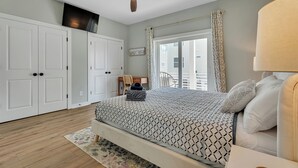A bedroom with a bed, a ceiling fan, a window with curtains, and a view of the outside. - Seaside Splendor! Rooftop Views, 3 Minute Walk to Beach (Carolina Beach)
