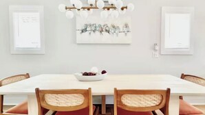 A dining area with a white table, wooden chairs with woven seats, and a chandelier. - Seaside Splendor! Rooftop Views, 3 Minute Walk to Beach (Carolina Beach)