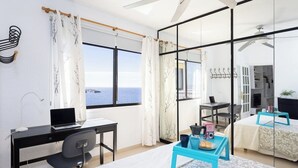 Ein modernes Hotelzimmer mit großem Fenster, einem Schreibtisch mit Laptop, einem Bett und einem kleinen Tisch mit Tablett.