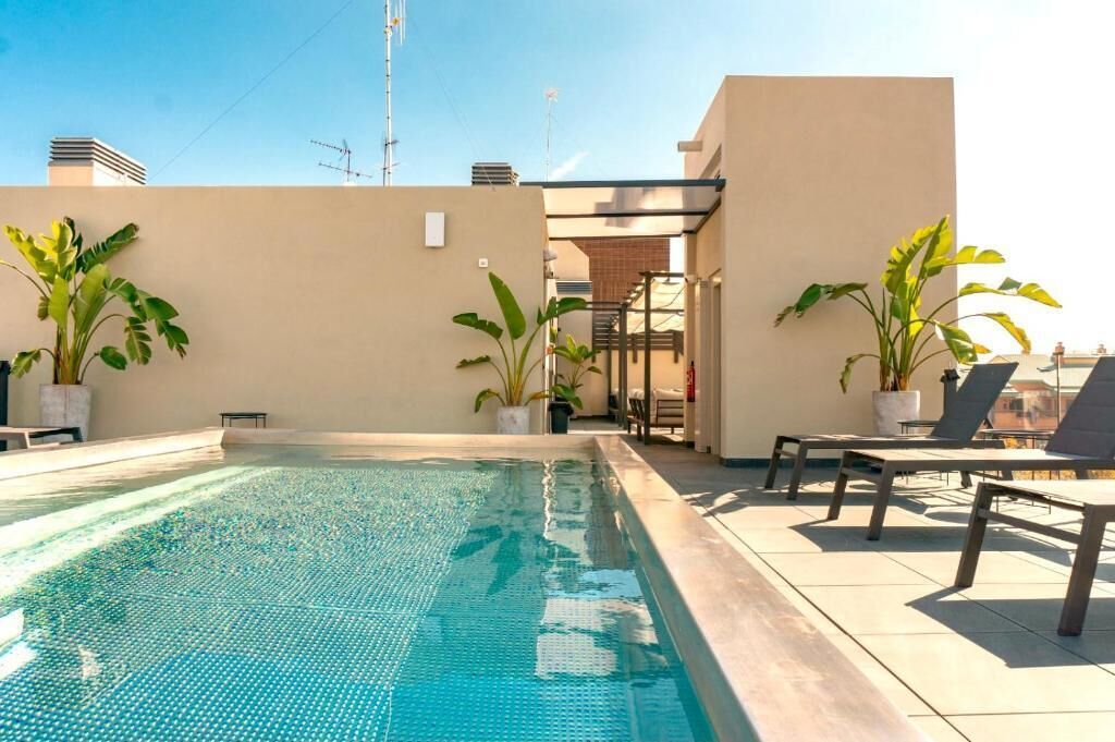 A rooftop pool with lounge chairs and potted plants.