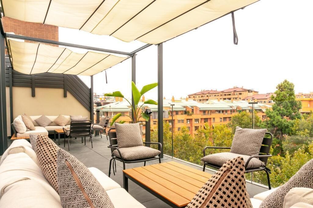 Terraza en la azotea con un sofá, sillas y una mesa, con vistas a un paisaje urbano.