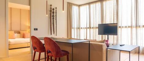 Una sala de estar moderna con un sofá, una mesa de comedor y dos sillas rojas. Hay un televisor sobre un mueble bajo y una lámpara sobre la mesa.