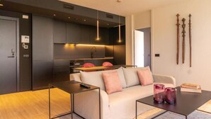 A modern living room with a sofa, coffee table, and a kitchen area with dark cabinetry and pendant lighting. - Valencia Luxury - Sea Port II (Valencia)