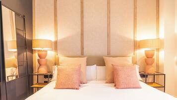 Una habitación de hotel con una cama grande, dos mesitas de noche con lámparas, un espejo y un cabecero con líneas verticales.