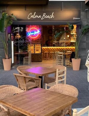 An outdoor seating area with wicker tables and chairs at a restaurant named "Calma Beach." - Valencia Luxury - Calma Beach Apartments (Valencia)