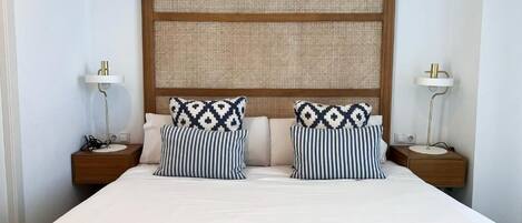 A neatly made bed with two pillows, a headboard with a woven panel, and bedside tables with lamps.