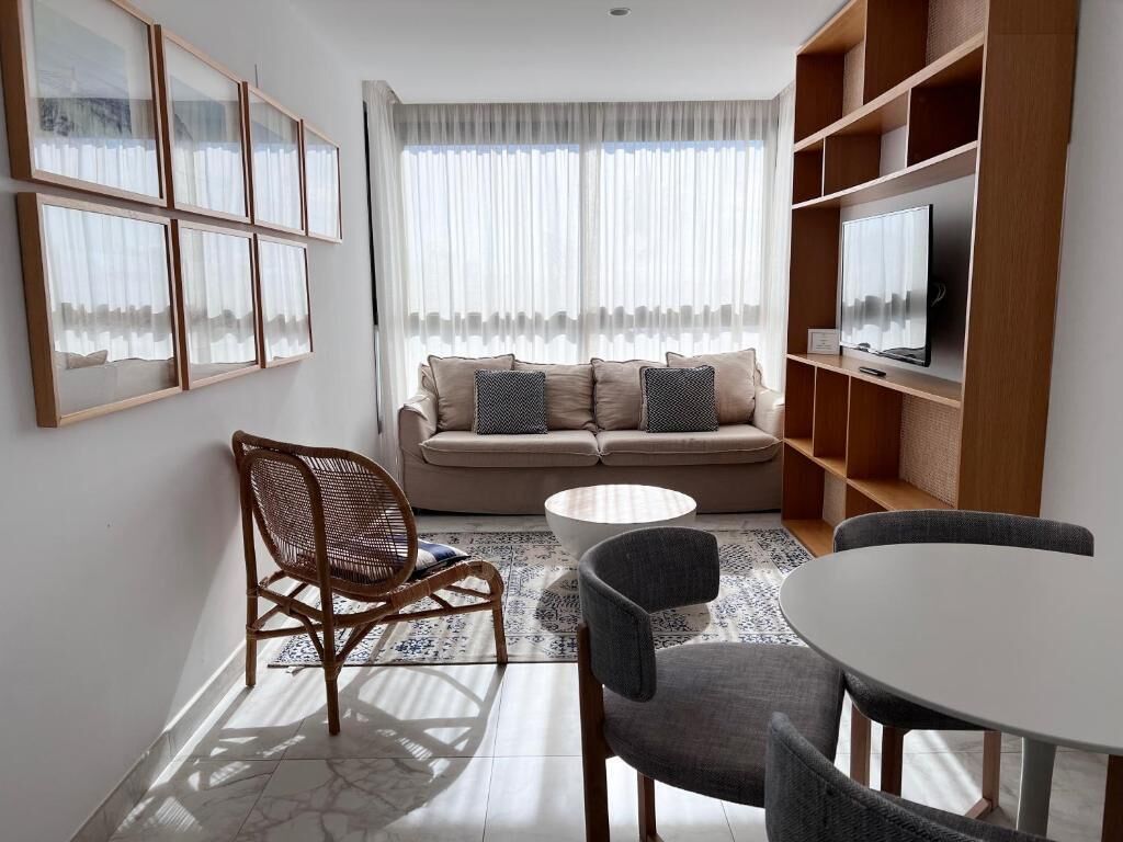 Un salon comprenant un canapé, deux fauteuils, une table basse et un téléviseur posé sur une étagère en bois.