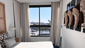 A hotel room with a large bed, a view of the city through a window, and a wall with wooden sculptures. - Valencia Luxury - Calma Beach Apartments (Valencia)