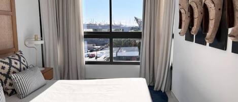 A hotel room with a large bed, a view of the city through a window, and a wall with wooden sculptures.