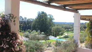 A covered outdoor area with a view of a swimming pool and surrounding greenery.