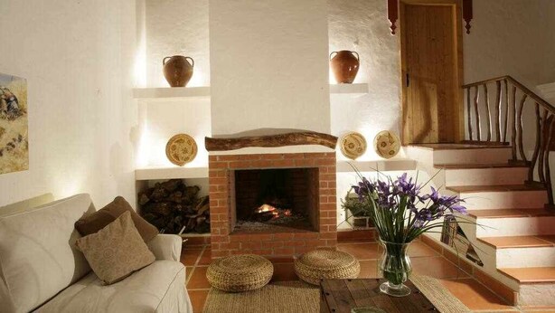 A living room with a fireplace, a sofa, a staircase, and decorative items on shelves.