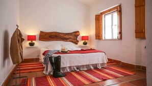 A bedroom with a wooden headboard, two bedside lamps, a bed with a red and white striped blanket, a hat, and a pair of boots on the floor.
