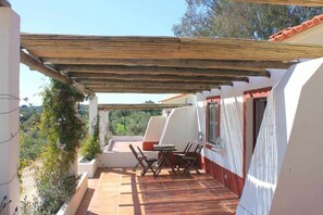 A covered outdoor patio with a table and chairs, surrounded by white walls and a wooden pergola. - Rabbit House (Azerveira)
