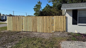 A wooden fence with metal brackets, a grassy area, and a building with a garage door.