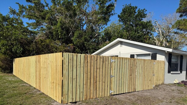 A fenced backyard with a house in the background.
