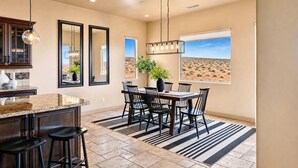A kitchen with a large island, dining area with chairs, and a view of the desert through a window. - The Overlook - Triple Primary Luxe, 50 Mile Views (Page)