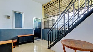 A staircase with a metal railing, a wooden bench, and a table in a room with tiled flooring and a high ceiling. - OYO Life 2928 Rumah Ceria (Semarang)