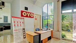 A hotel reception area with a wooden desk, a large window, and a poster on the wall. - OYO Life 2928 Rumah Ceria (Semarang)
