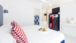 Ein modernes Hotelzimmer mit einem ordentlich bezogenen Bett, einem kleinen Frühstücksbrett und einem Kleiderständer mit aufgehängter Kleidung.