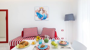 Ein modernes, minimalistisches Zimmer mit einer weiß-rot gestreiften Sofagarnitur, einem Tisch mit Frühstücksangeboten und einer Wandlampe.