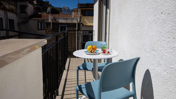 Ein Balkon mit Tisch und Stühlen, ein Teller mit Früchten und ein Glas mit Getränk.