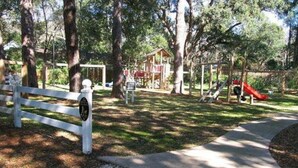 A park with a playground, a white fence, and a paved path. - L3, downstairs Oceanwalk/remodeled (St. Simons Island)