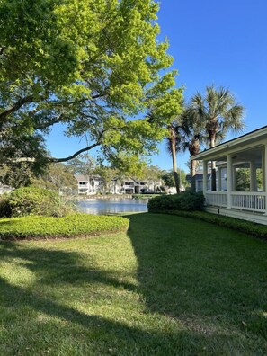 A well-maintained lawn, a covered porch, and a body of water in the background.