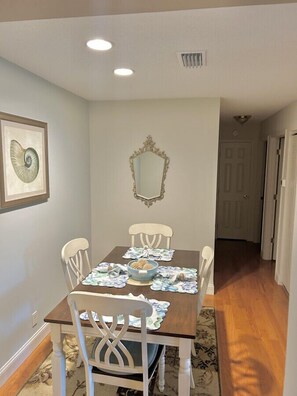A dining room with a wooden table, four chairs, a decorative mirror, and a framed artwork on the wall. - L3, downstairs Oceanwalk/remodeled (St. Simons Island)