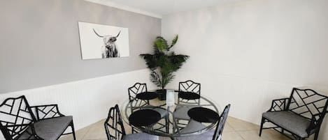 Uma sala de jantar com uma mesa redonda de vidro rodeada por cadeiras pretas com padrões geométricos.
