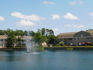 A tranquil lake with a fountain, surrounded by residential buildings and lush greenery. - K5 corner townhome next to lake, tidy and ready for your vacation! (Saint Simons Island)