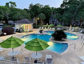 A swimming pool area with multiple lounge chairs and umbrellas, surrounded by trees and a small building. - O1 Two BR townhome in Ocean Walk with 1 king, 1 queen bed.  Recently updated. (Saint Simons Island)