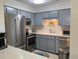 Una cocina compacta con armarios grises, un refrigerador de acero inoxidable, un microondas, un tostador y una cafetera.