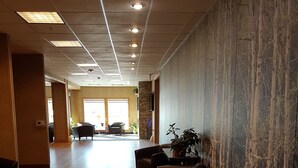 A spacious lobby with wooden flooring, a seating area with armchairs, a wall with a tree pattern mural, and recessed ceiling lighting. - Target Hospitality-Cheecham Lodge (Janvier South)